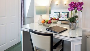 Camera d'albergo con zona pranzo che include un tavolo in vetro, una sedia, una ciotola di frutta, una lampada e un'orchidea in vaso.