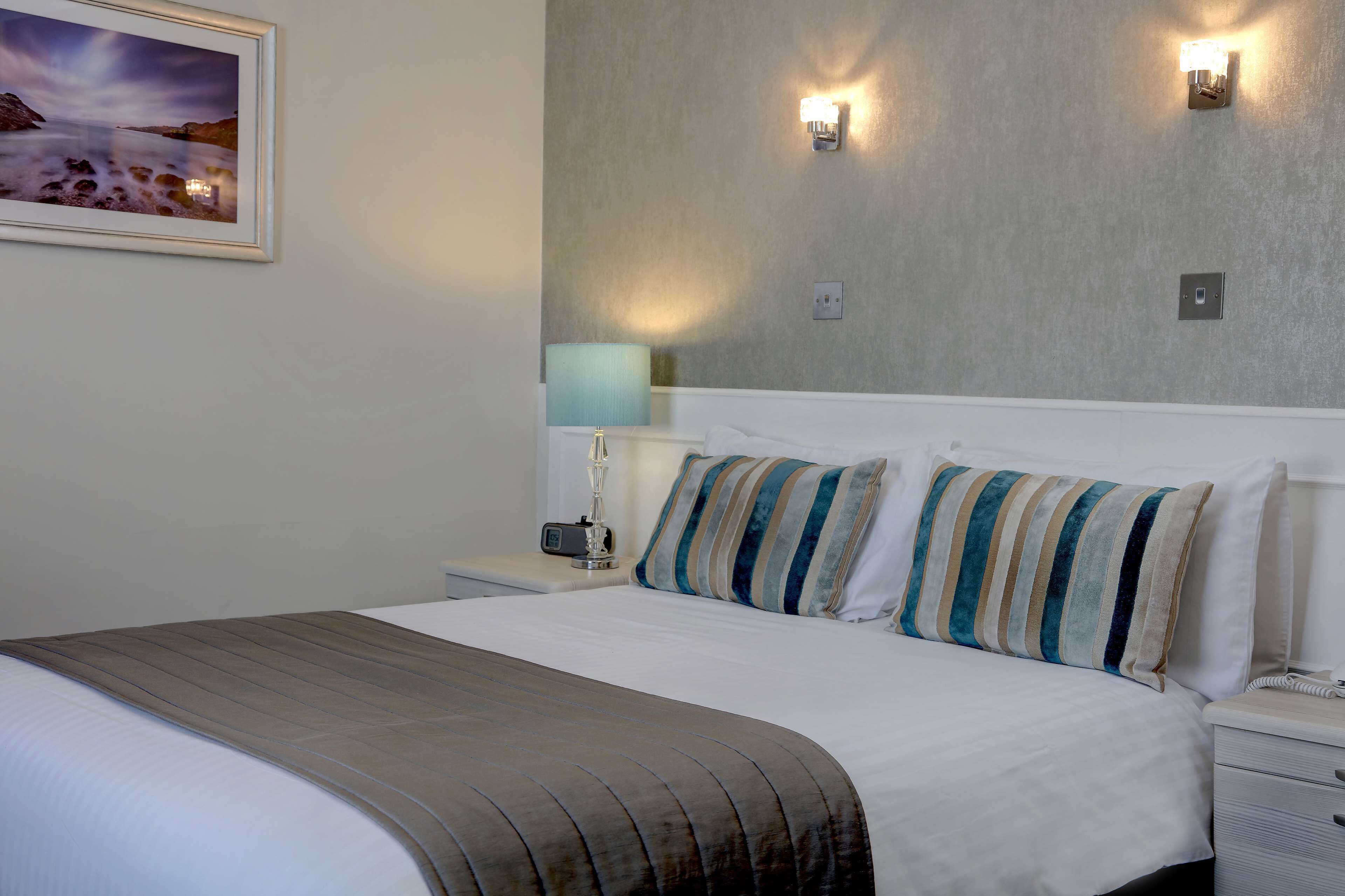 A neatly made bed with striped pillows, a bedside lamp, and a framed picture on the wall.