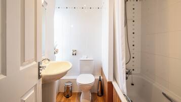 A compact bathroom with a sink, toilet, and shower.