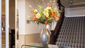 Una scalinata con tappeto a righe, un tavolino in vetro con un vaso di fiori e un lampadario.