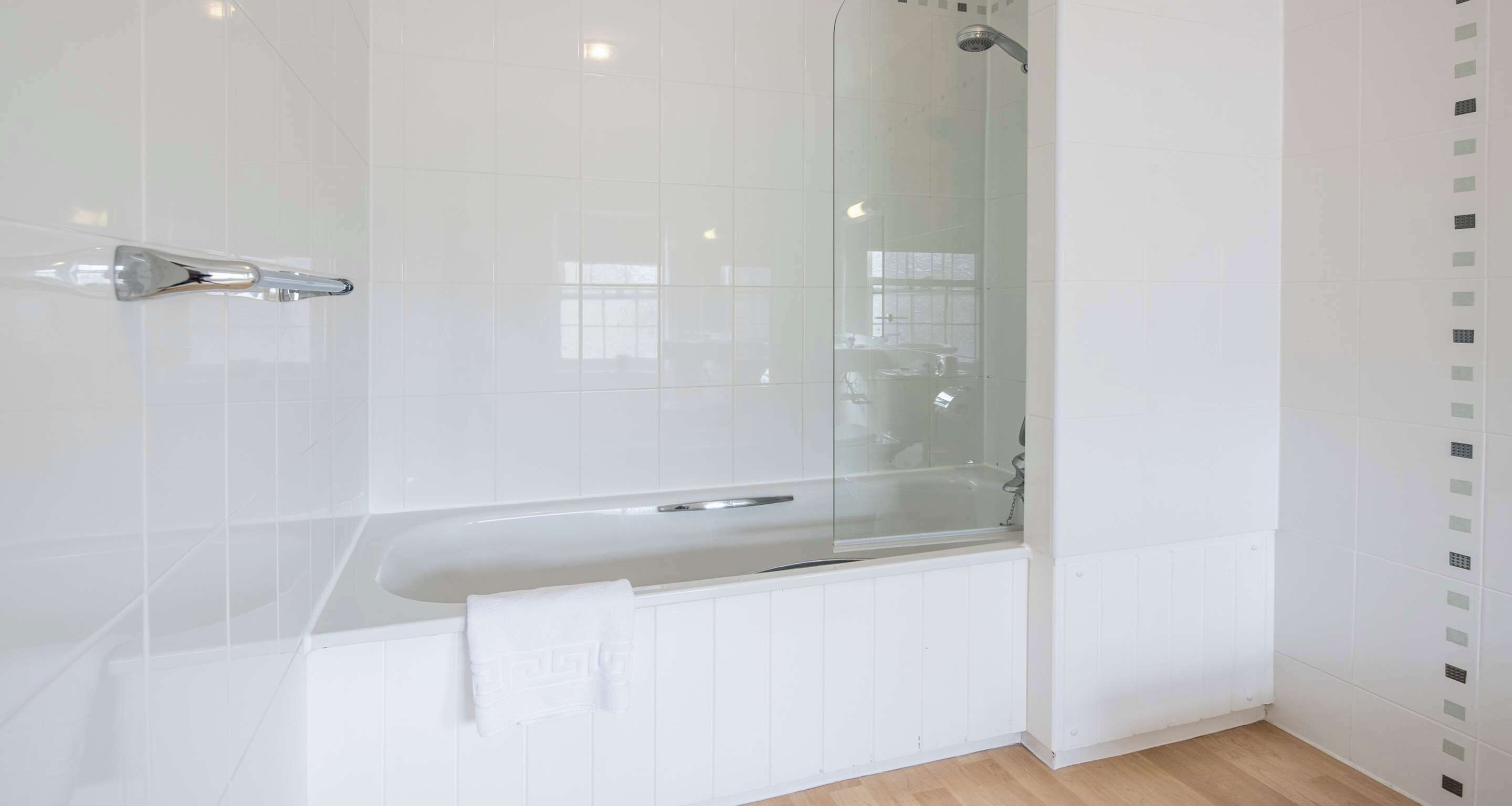A modern bathroom with a glass-enclosed shower, white tiles, and a wooden floor.