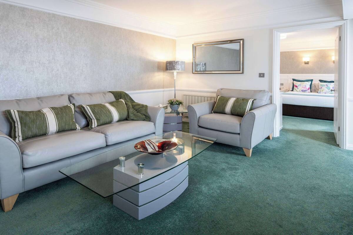 A modern living room with a grey sofa set, a glass coffee table, and a green carpet.