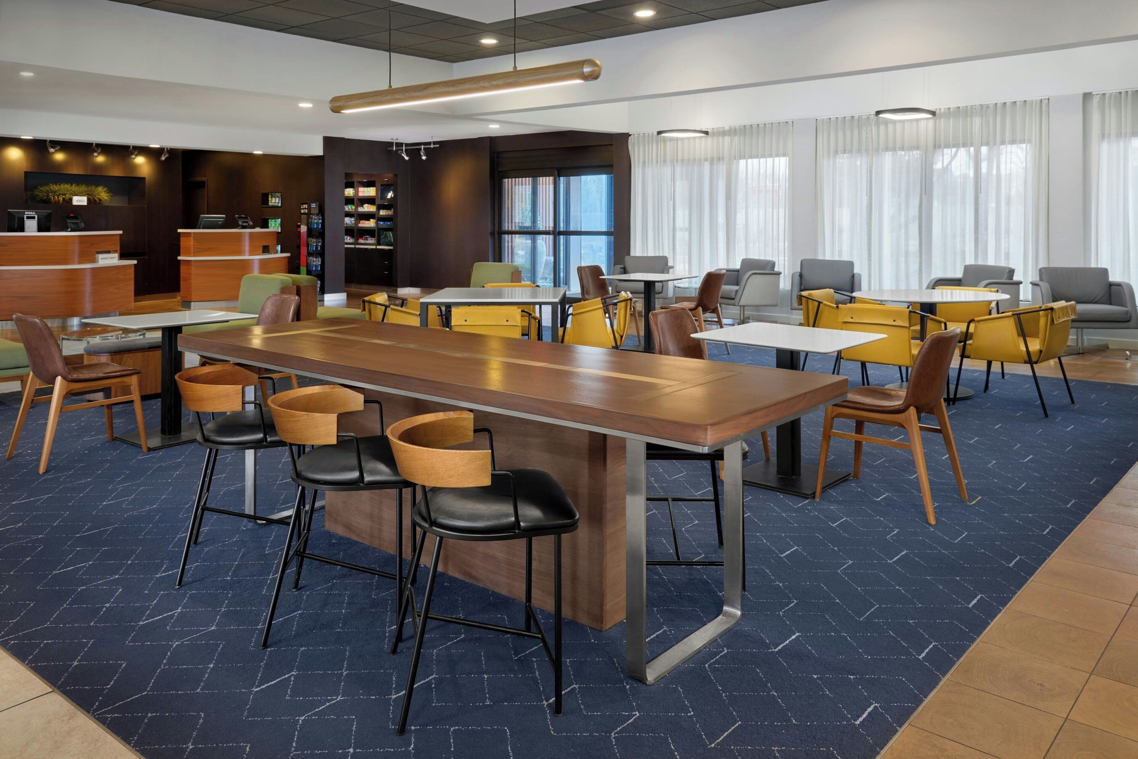 Eine moderne Hotellobby mit einer zentralen Essecke, einer Rezeption und einem Bücherregal.