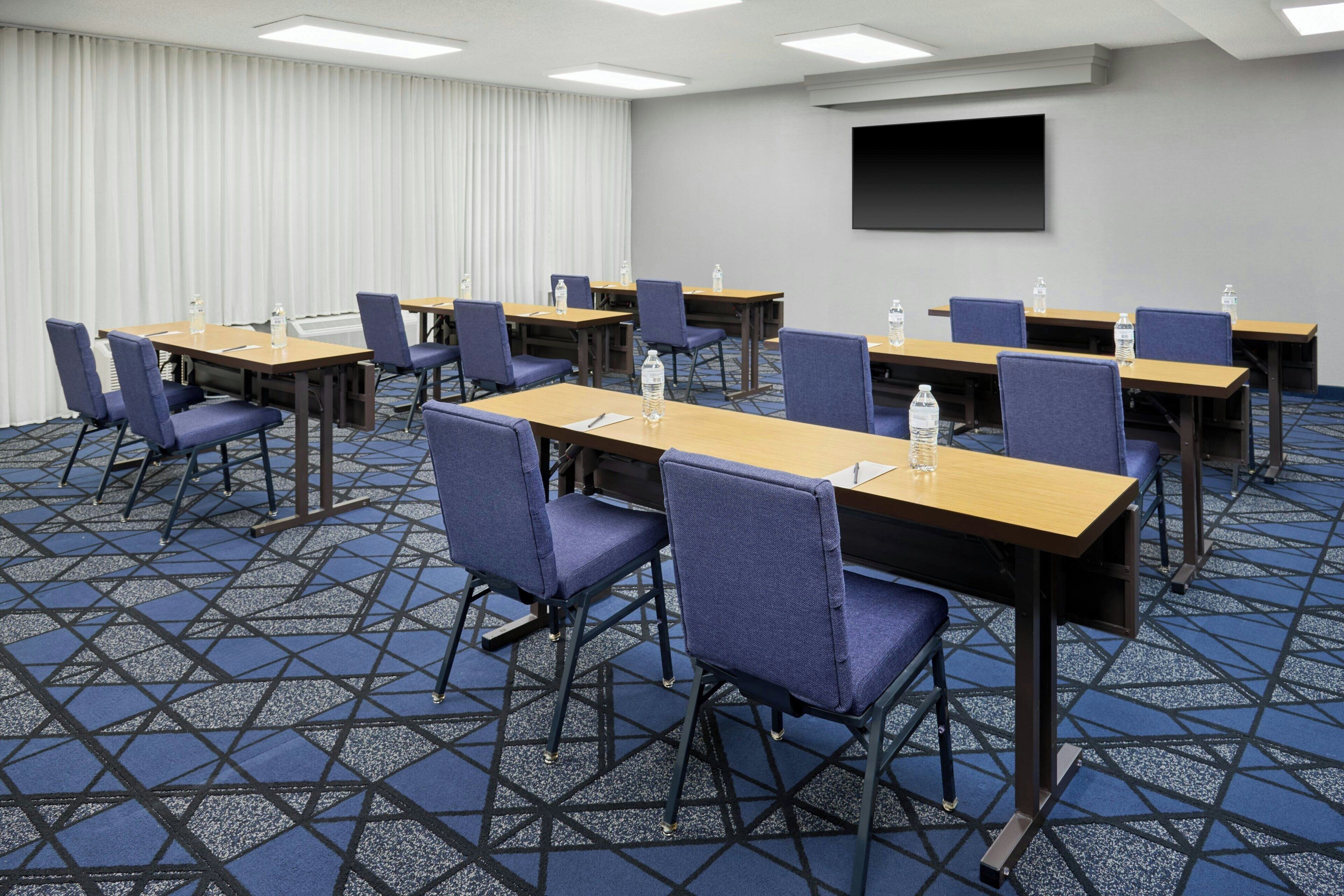 A conference room with multiple tables and chairs, equipped with water bottles, and a flat-screen TV on the wall.