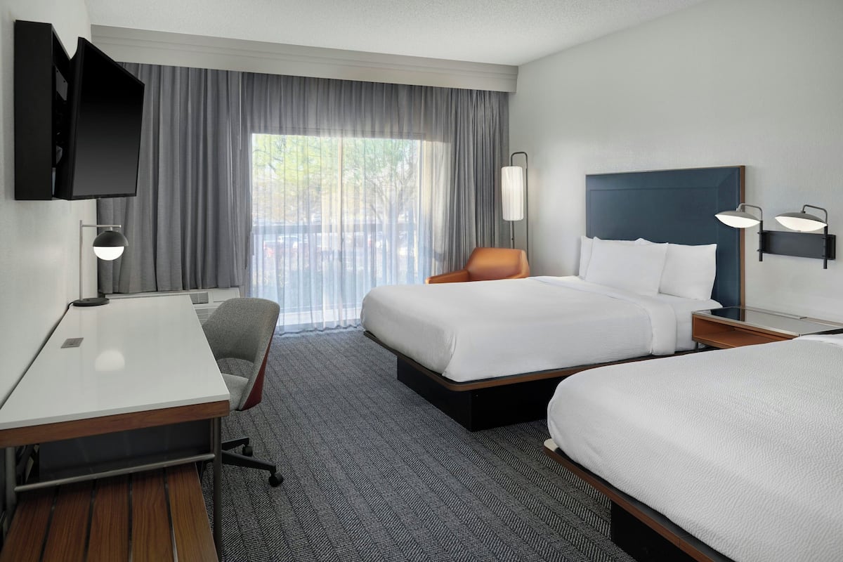 A hotel room with a bed, a desk, a chair, a TV, and a window with curtains.