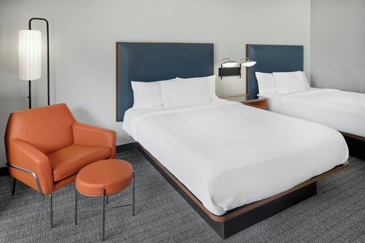 A hotel room with two beds, a chair, a lamp, and a carpeted floor.