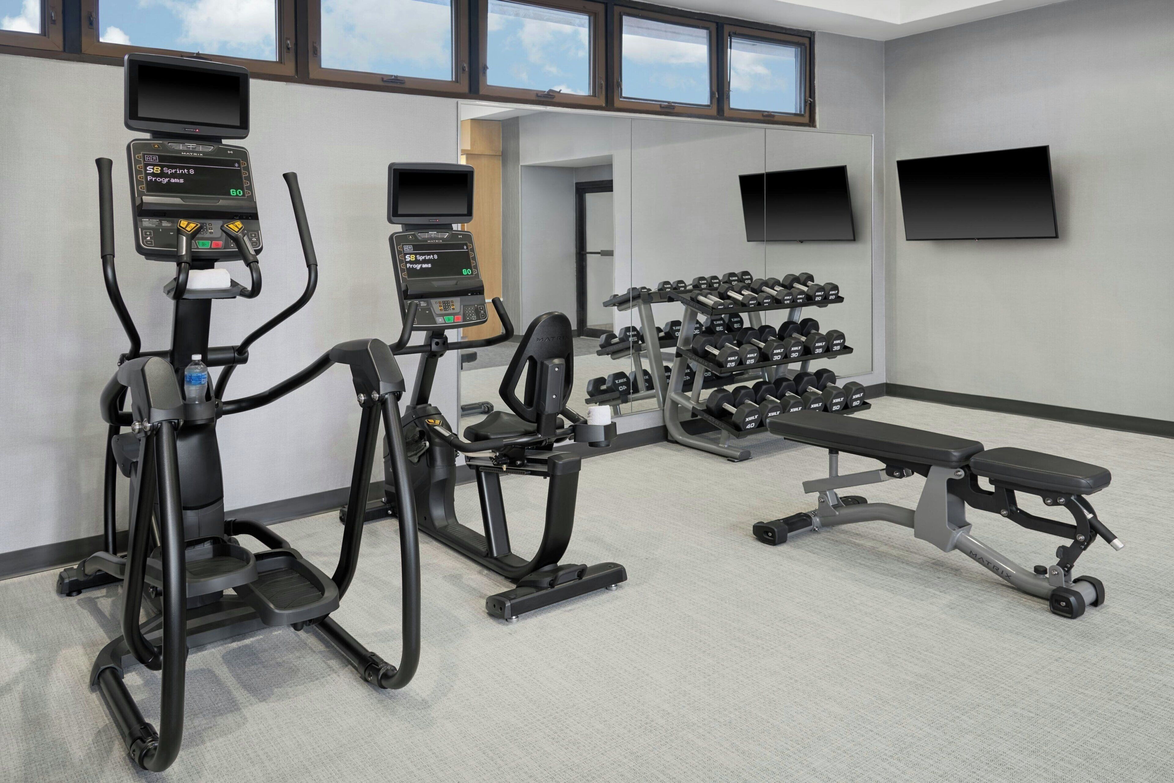 A gym with treadmills, a bench, and dumbbells.