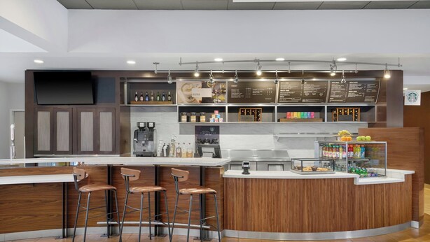 A modern coffee shop with a wooden counter, bar stools, and a menu board. - Courtyard by Marriott Huntsville University Drive (Huntsville)
