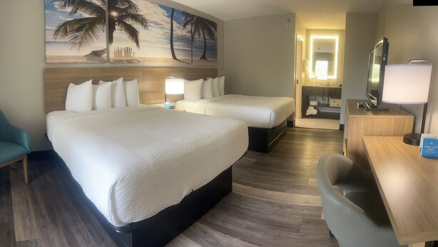 Habitación de hotel con dos camas, un escritorio, una silla y un cuadro grande con motivos playeros.