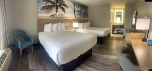 Habitación de hotel con dos camas, un escritorio, una silla y un cuadro grande con motivos playeros.