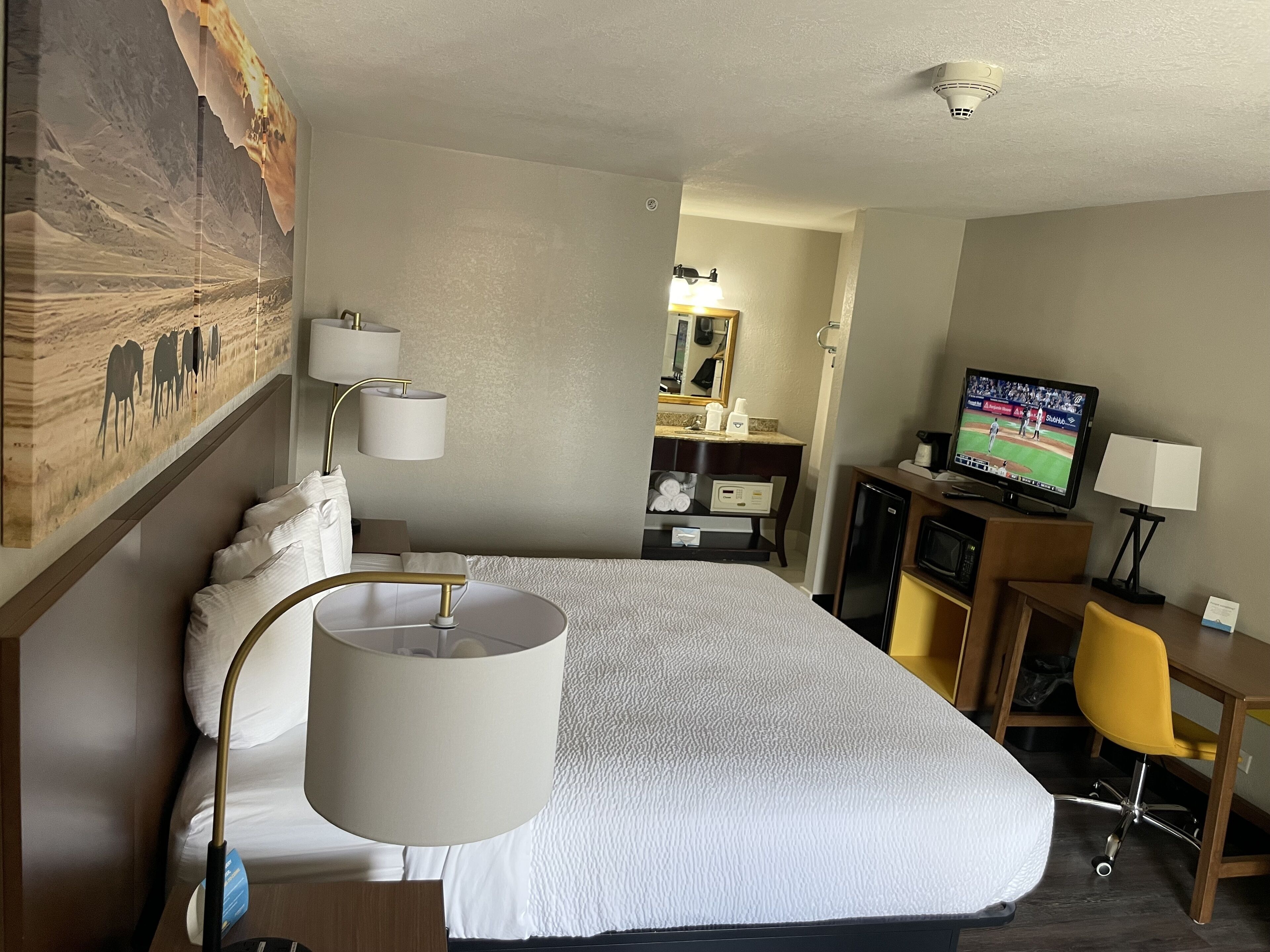 A hotel room with a large bed, a desk with a chair, a television, and a painting on the wall.