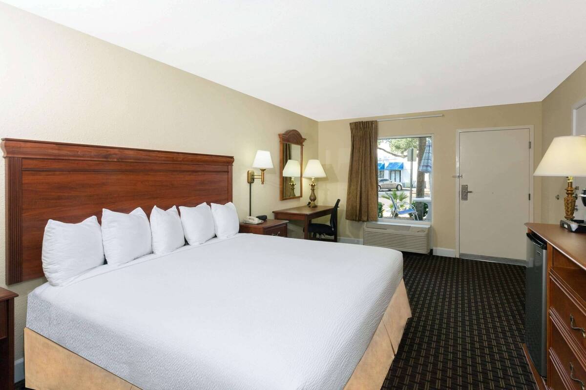 Habitación de hotel con una cama grande, un escritorio, una silla, un espejo, una lámpara y una ventana con cortinas.