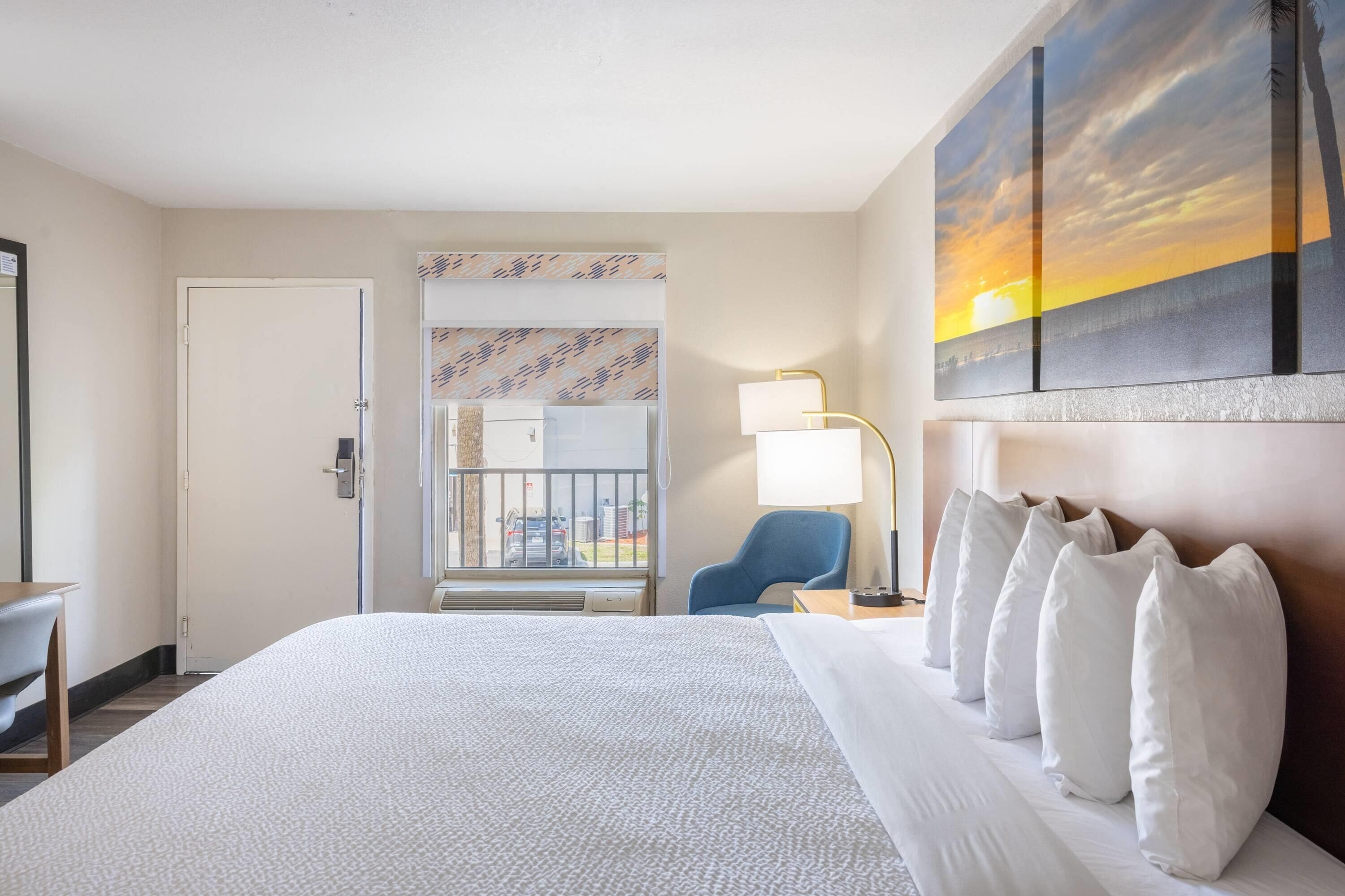 Habitación de hotel con una cama grande, un escritorio, una silla, un balcón con vistas y un cuadro en la pared.