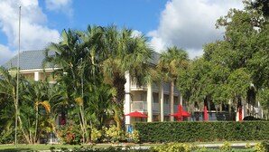 Un hotel con fachada blanca, sombrillas rojas y abundante vegetación.