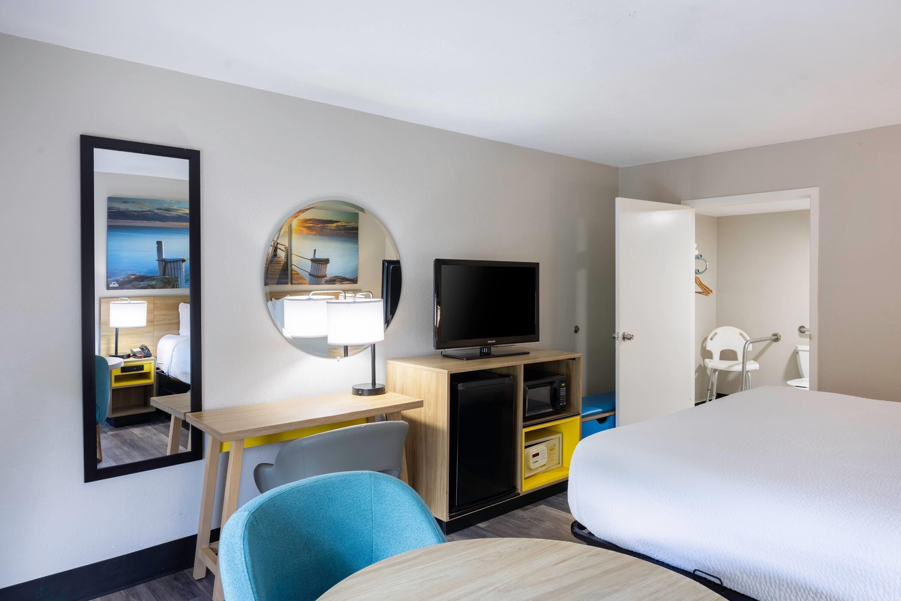 Habitación de hotel con cama, escritorio con televisor, espejo y vista al mar.