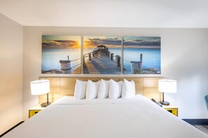 A hotel room with a large bed, two bedside lamps, and a wall with three paintings of a pier.