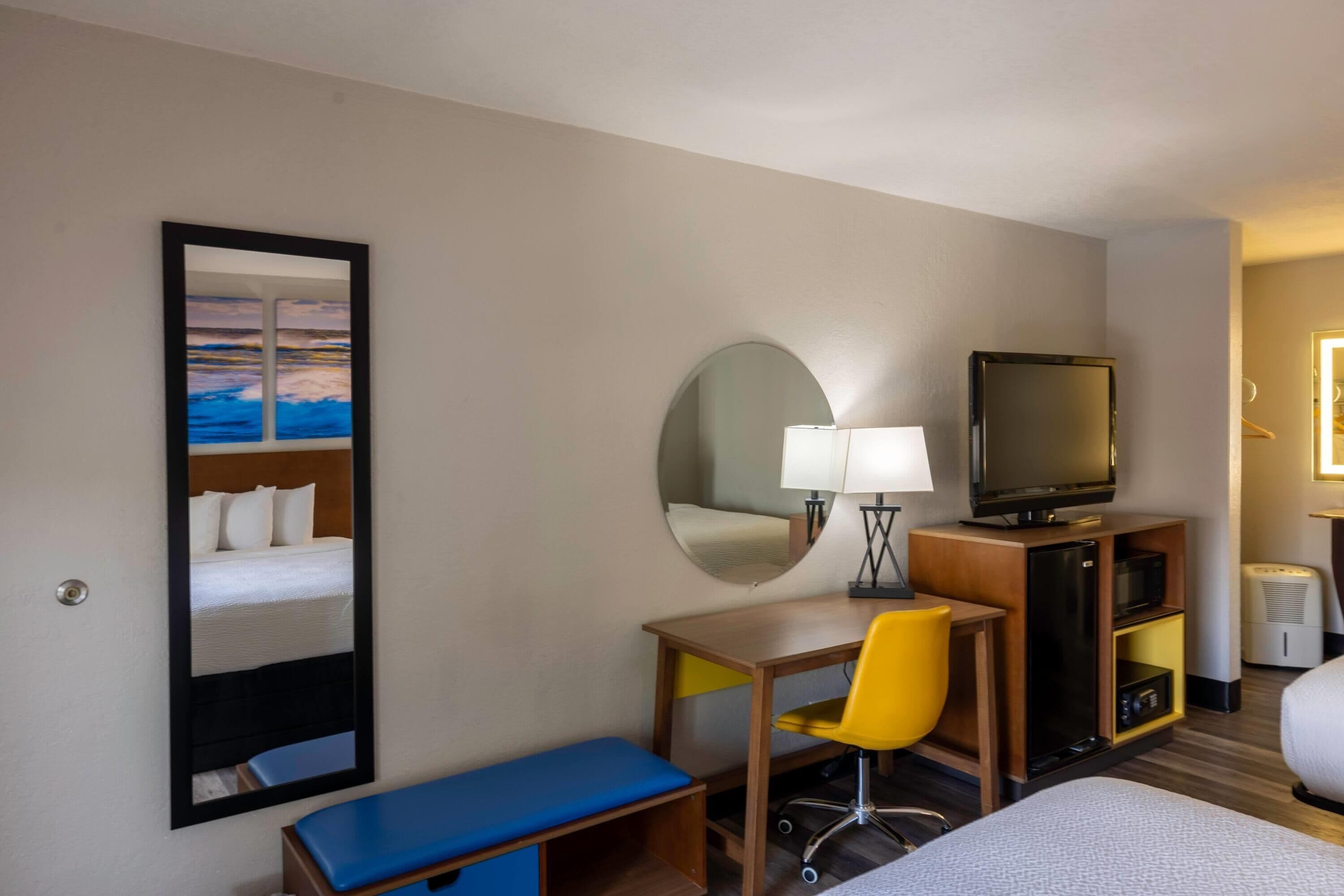 A hotel room with a bed, a desk, a chair, a television, a mirror, and a window.