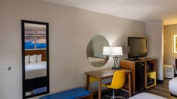 Habitación de hotel con cama, escritorio, silla, televisor, espejo y ventana.