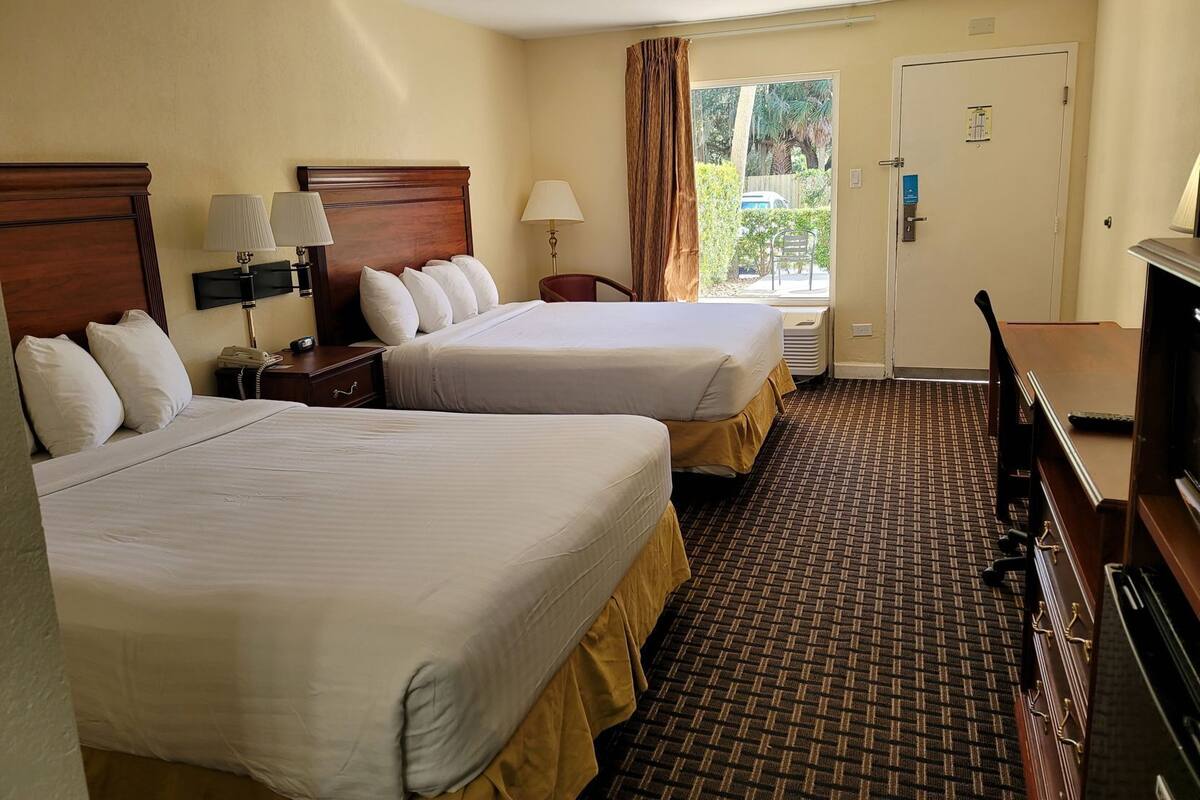 Habitación de hotel con dos camas, un escritorio, una silla, un televisor y una ventana con cortinas.