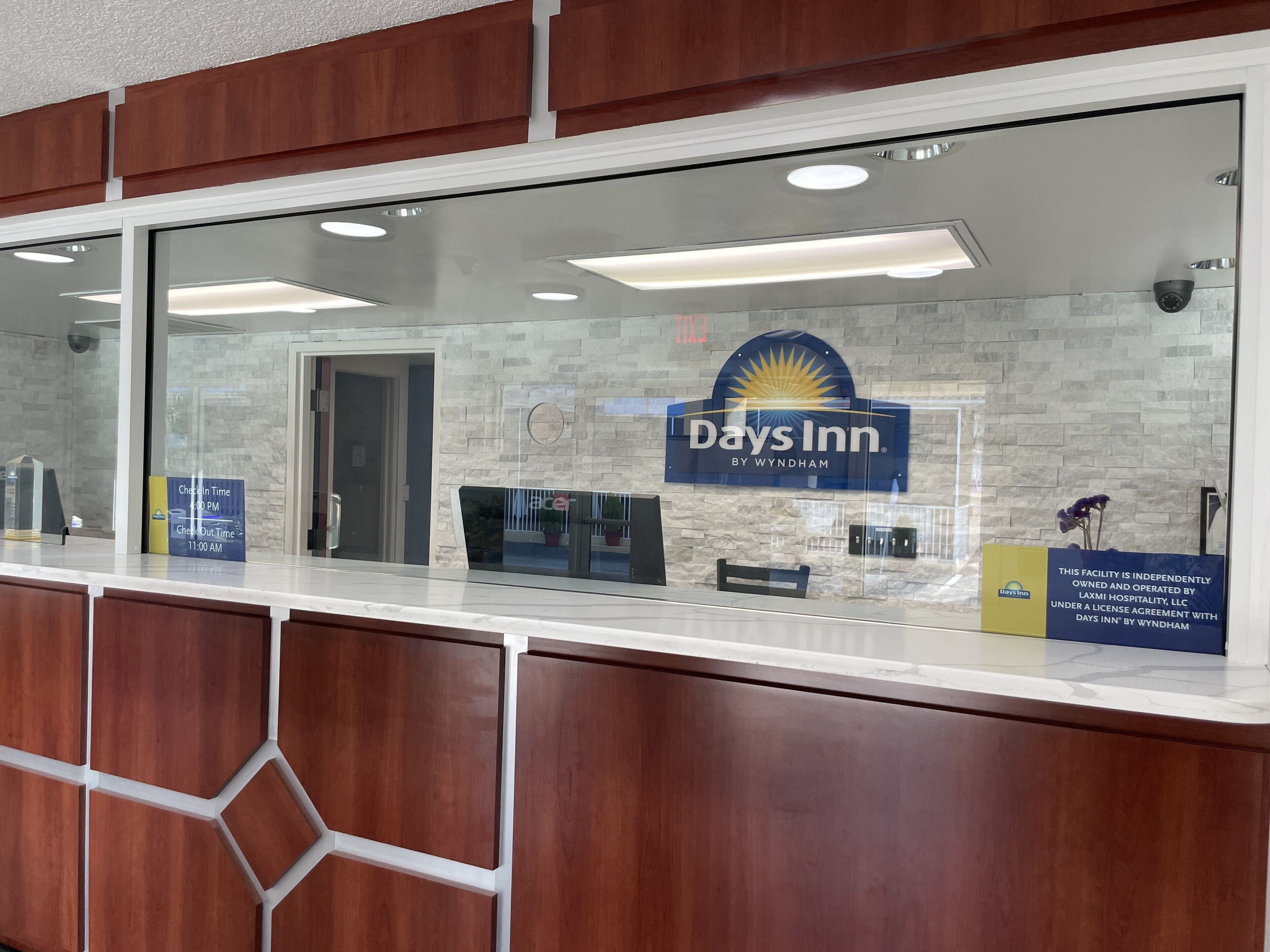 Un comptoir d’accueil dans un hôtel Days Inn by Wyndham, avec un mur en pierre en arrière-plan, une enseigne bleue et un panneau indiquant les heures d’arrivée et de départ.