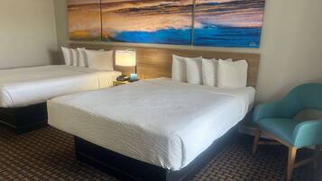 A hotel room with two beds, a nightstand with a lamp, a chair, and a large painting of a seascape on the wall.