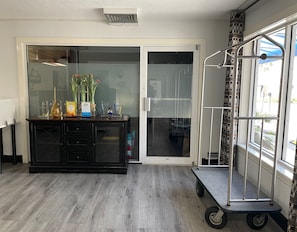 A hotel lobby with a reception desk, a glass door entrance, a metal cart, and a view of the outside.