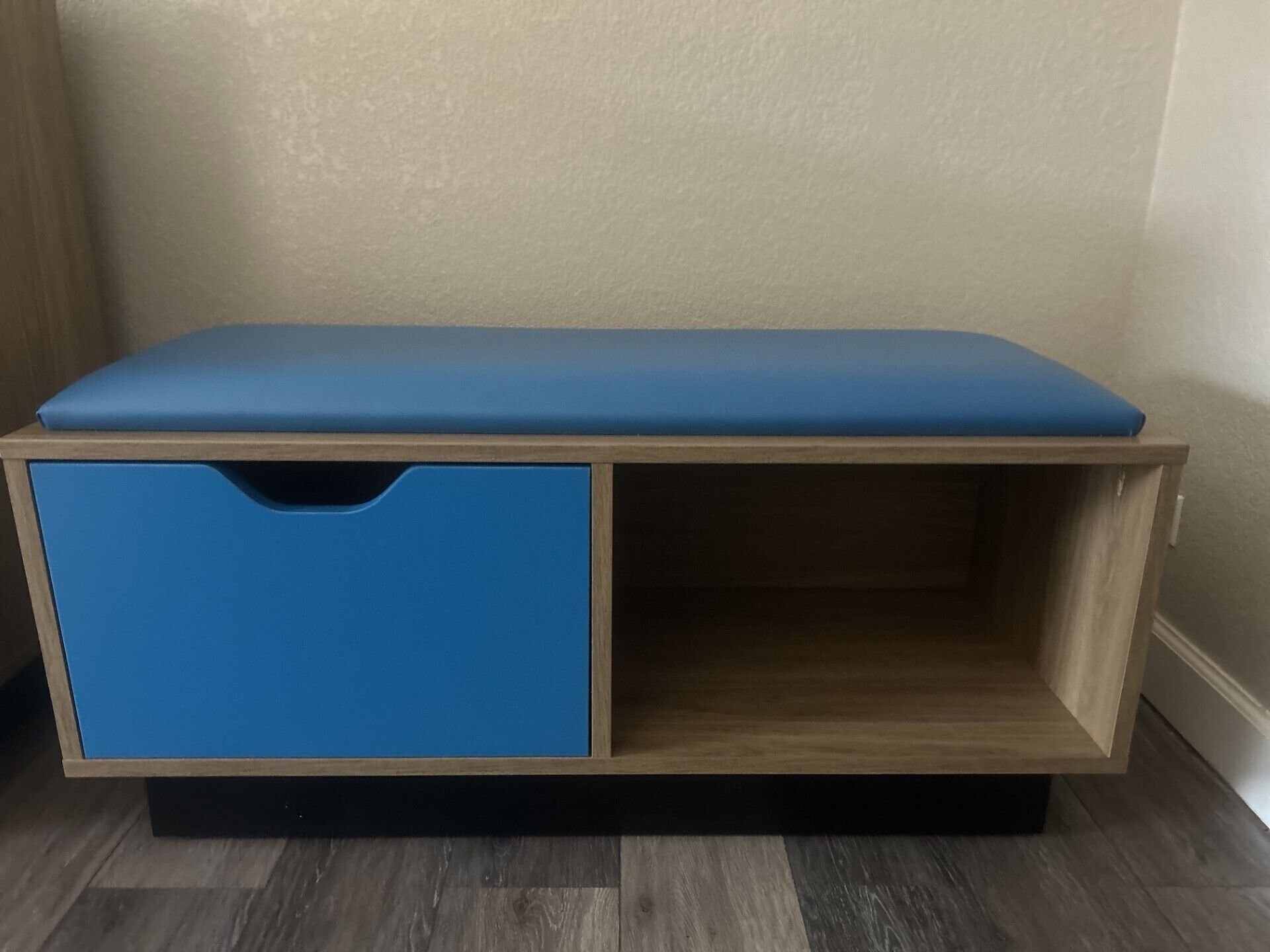A wooden bench with a blue cushioned top and a blue storage drawer.