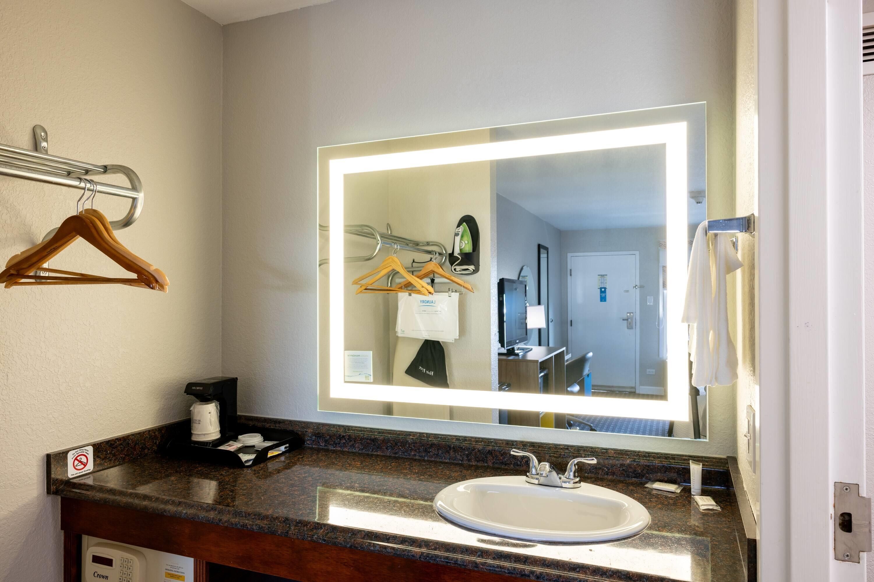 A hotel bathroom with a large mirror, a sink, a towel rack, and a coffee maker.