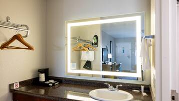 A hotel bathroom with a large mirror, a sink, a towel rack, and a coffee maker.