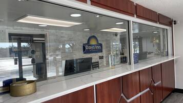 Un área de recepción con un separador de vidrio, un letrero de Days Inn y un monitor de computadora.