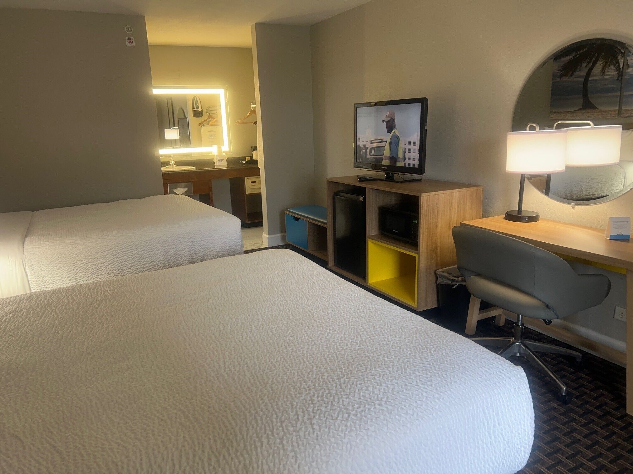 Habitación de hotel con dos camas, un escritorio con computadora, un televisor y una lámpara.