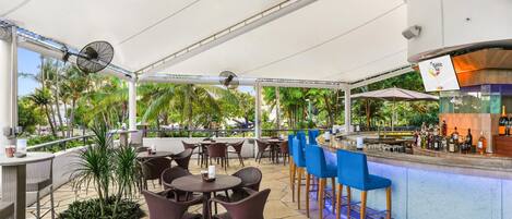 An outdoor bar area with wicker furniture, a bar counter, and a view of palm trees.