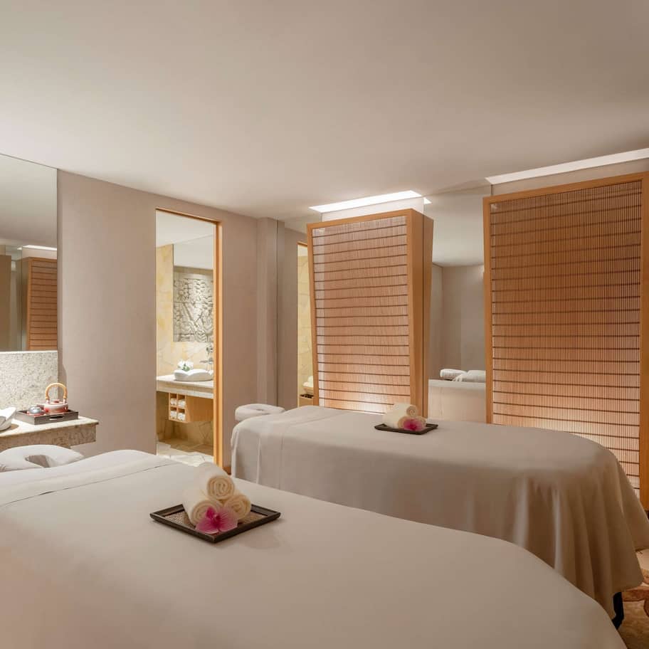 A hotel room with a large mirror, a sink, two beds with towels, and a potted orchid.