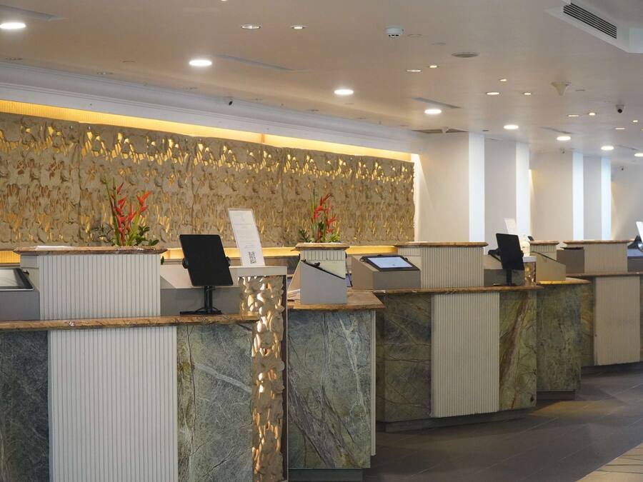 A modern hotel reception area with marble counters, a decorative wall, and a view of the lobby.