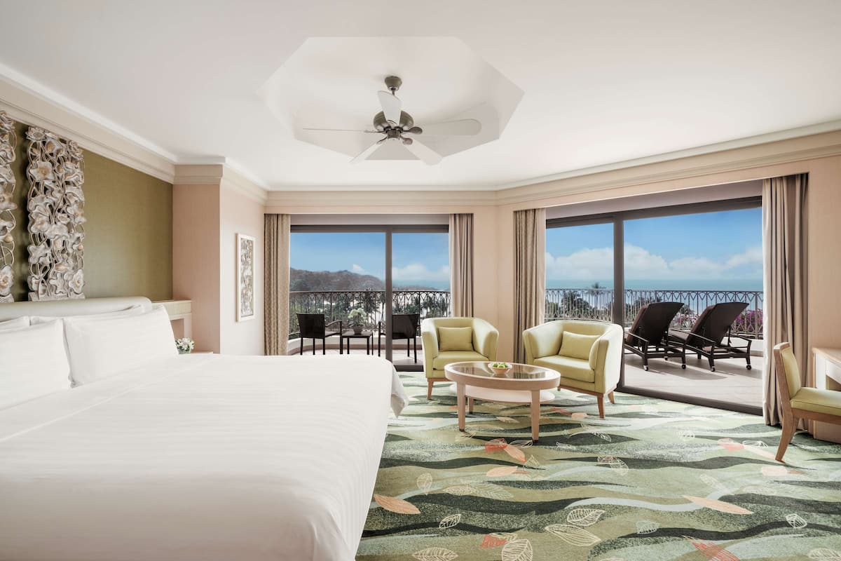 A hotel room with a large bed, a balcony with seating, and a view of the mountains.