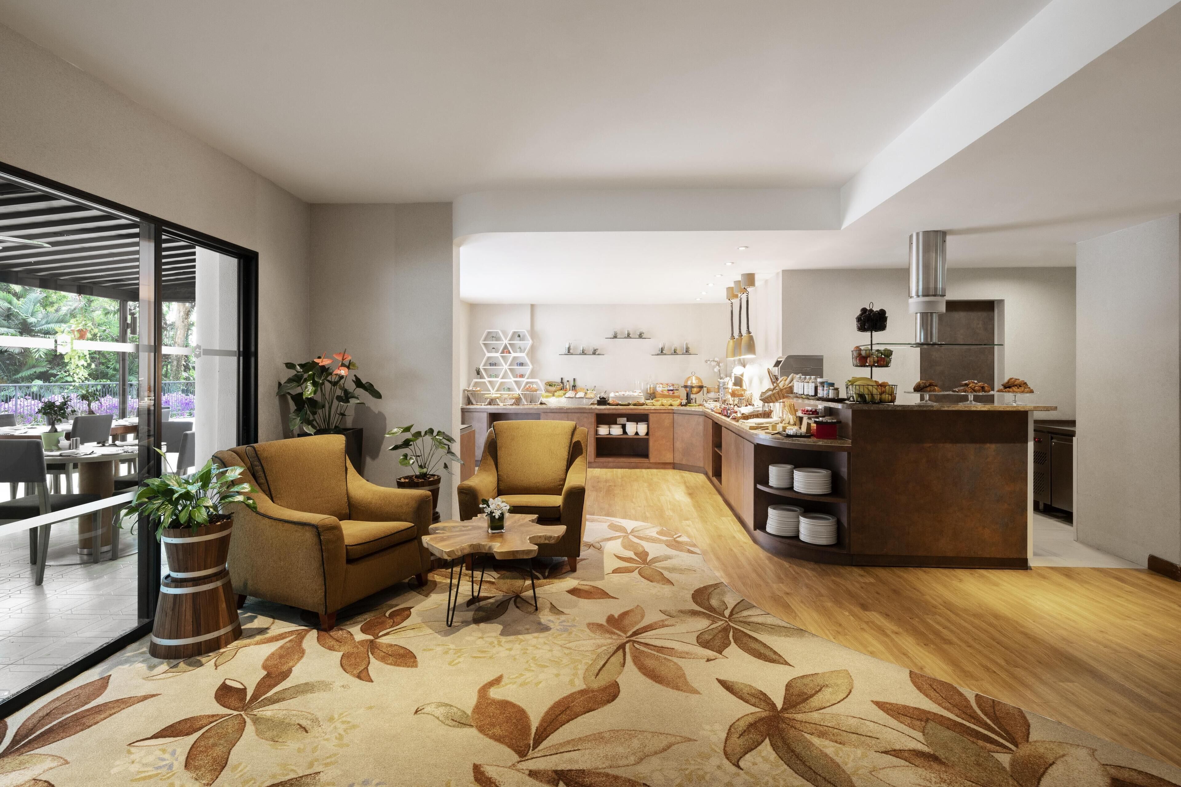 A modern living room with a sofa, coffee table, and potted plants. A kitchen area with a counter and cabinets is visible in the background.