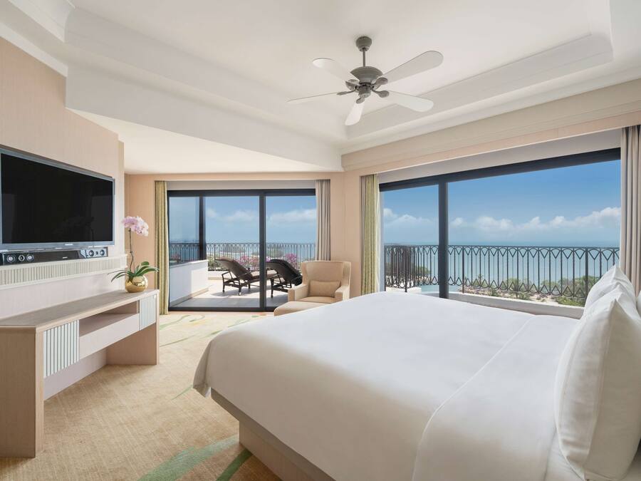 Habitación de hotel con una cama grande, televisión de pantalla plana, ventilador de techo y balcón con vistas.