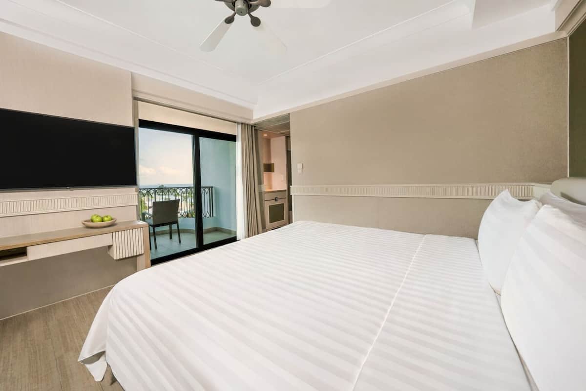 A hotel room with a bed, a TV, a desk with a bowl of fruit, and a balcony with a chair.