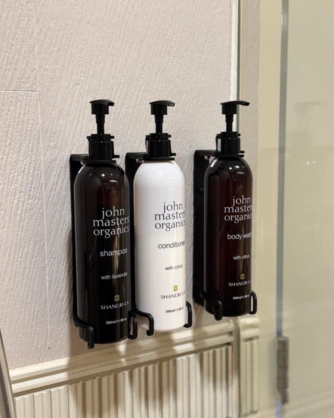 Tres botellas de productos John Masters Organics sobre una encimera de baño.