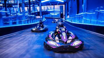 Go-karts racing in a brightly lit indoor track with a modern industrial design.