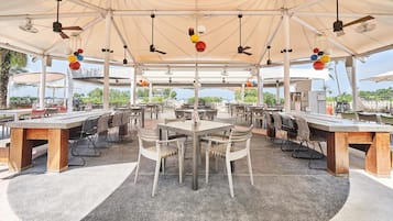 An outdoor dining area with tables and chairs, ceiling fans, and hanging spherical lights.