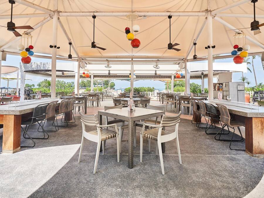 An outdoor dining area with tables and chairs, ceiling fans, and hanging spherical lights.