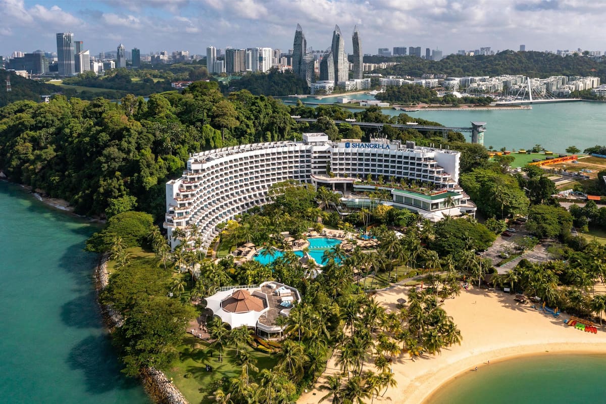 A large resort with a crescent-shaped building, multiple swimming pools, and a beach.