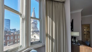 A hotel room with a large window offering a view of a historic building and modern skyscrapers. - Thistle London Holborn (London)