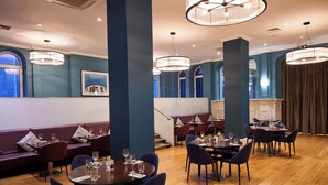 A restaurant with round tables, purple chairs, and blue walls. - Thistle London Holborn (London)