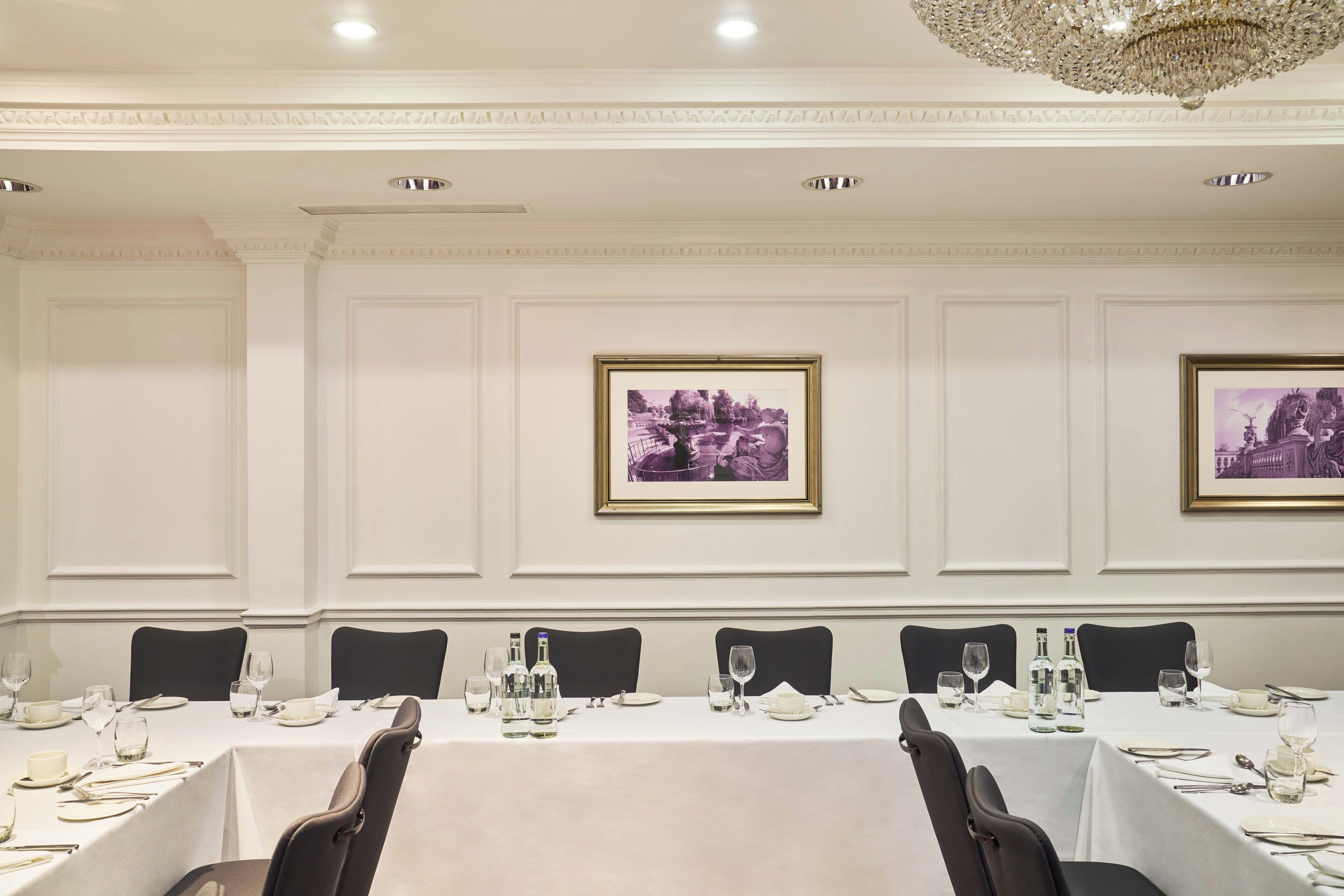 A conference room with a long table set for a meeting, framed pictures on the walls, and a chandelier above.