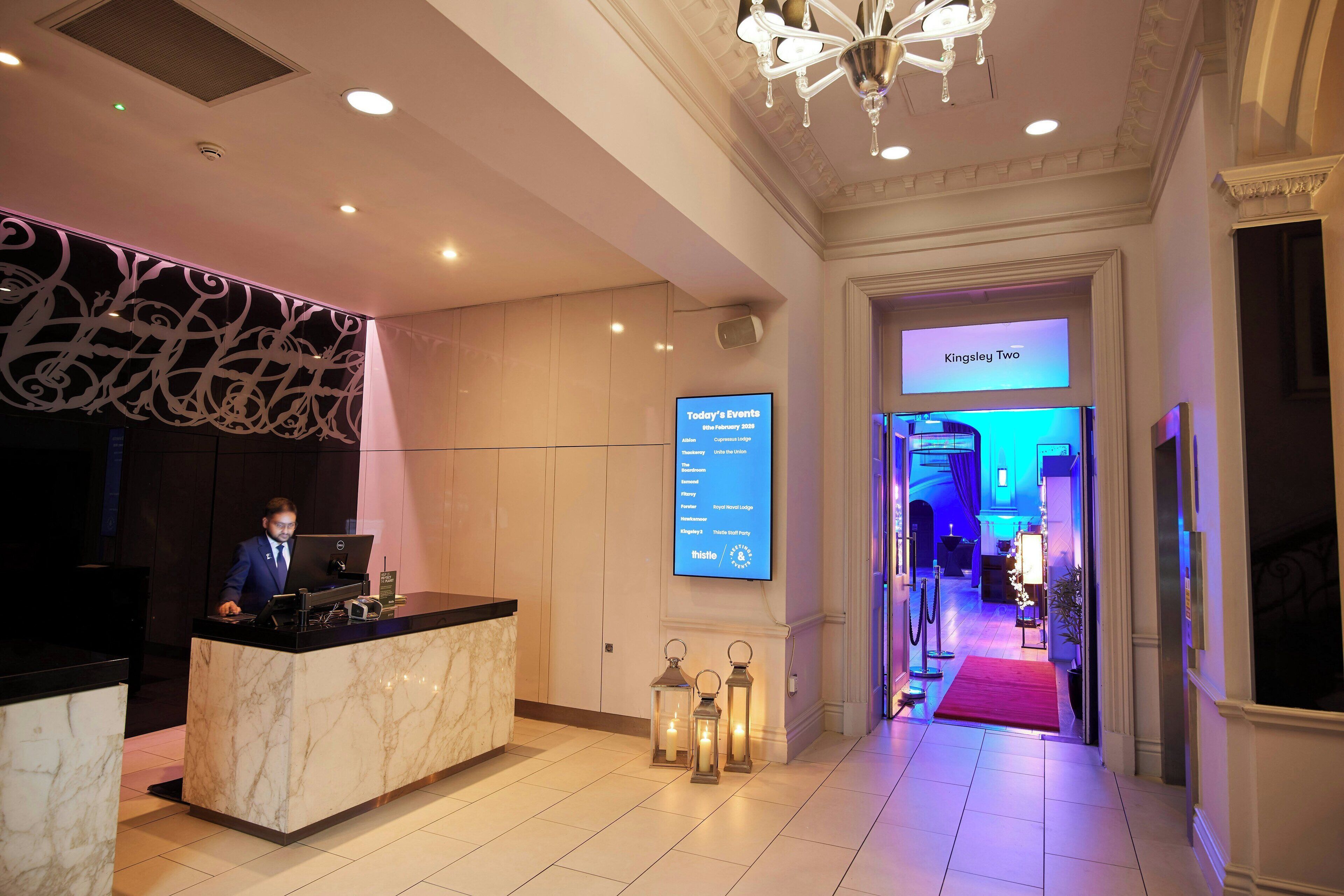 En hotellobby med en marmordisk, en digital skärm som visar aktuella evenemang och en kristallkrona.