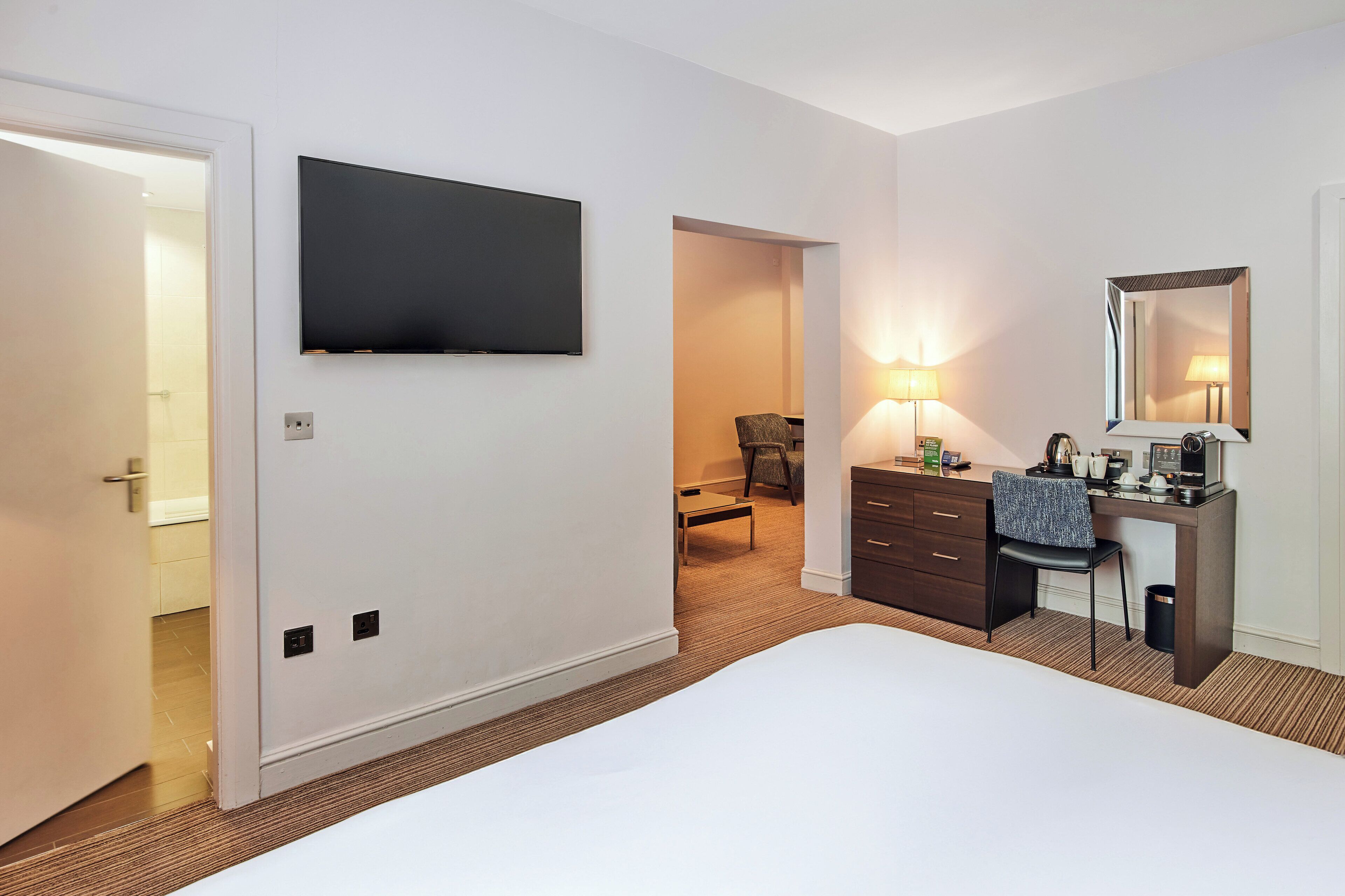 Een hotelkamer met een bed, een bureau, een stoel, een televisie en een spiegel.
