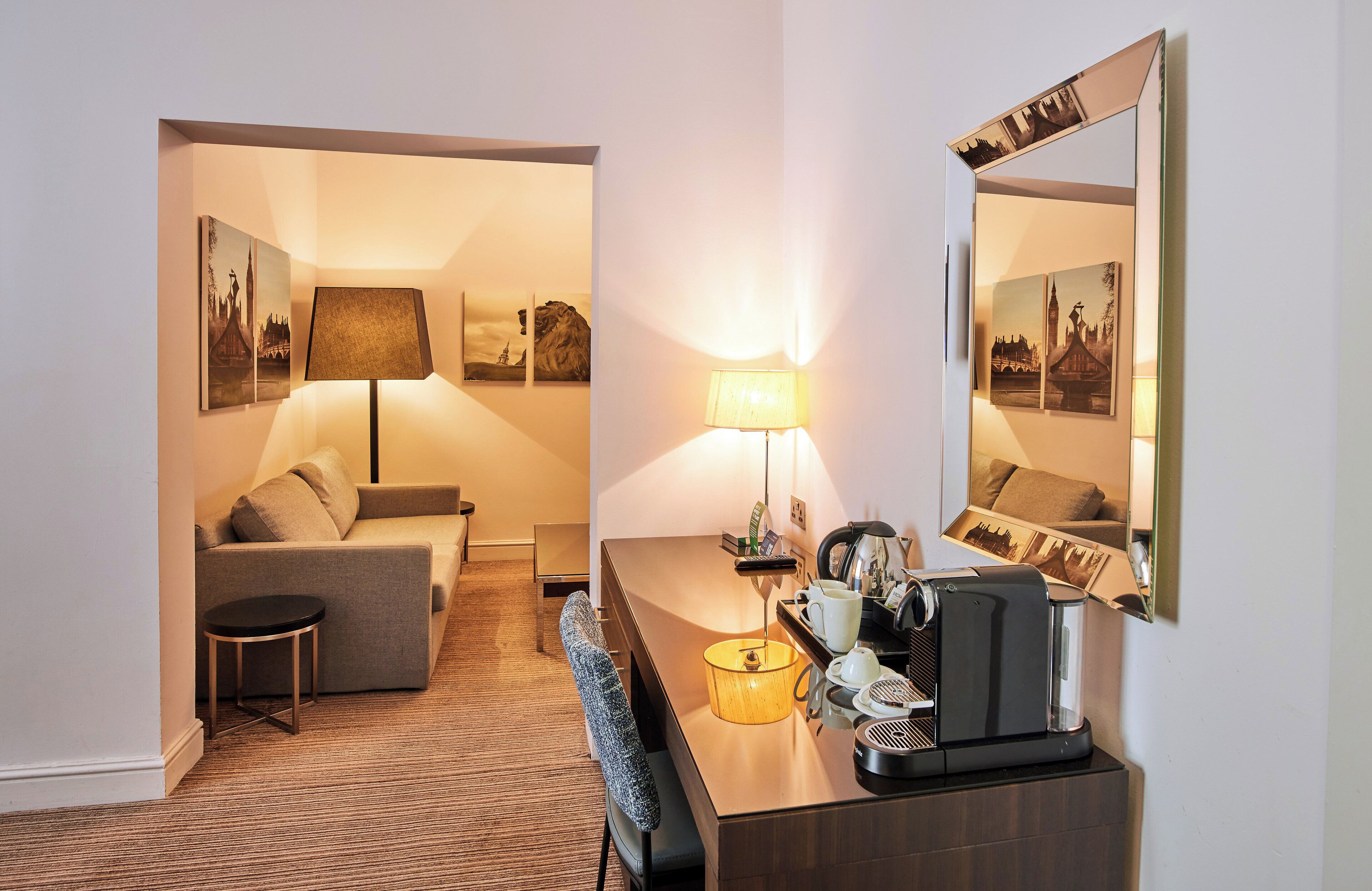 A hotel room with a sofa, a small round table, a coffee machine, and a lamp.