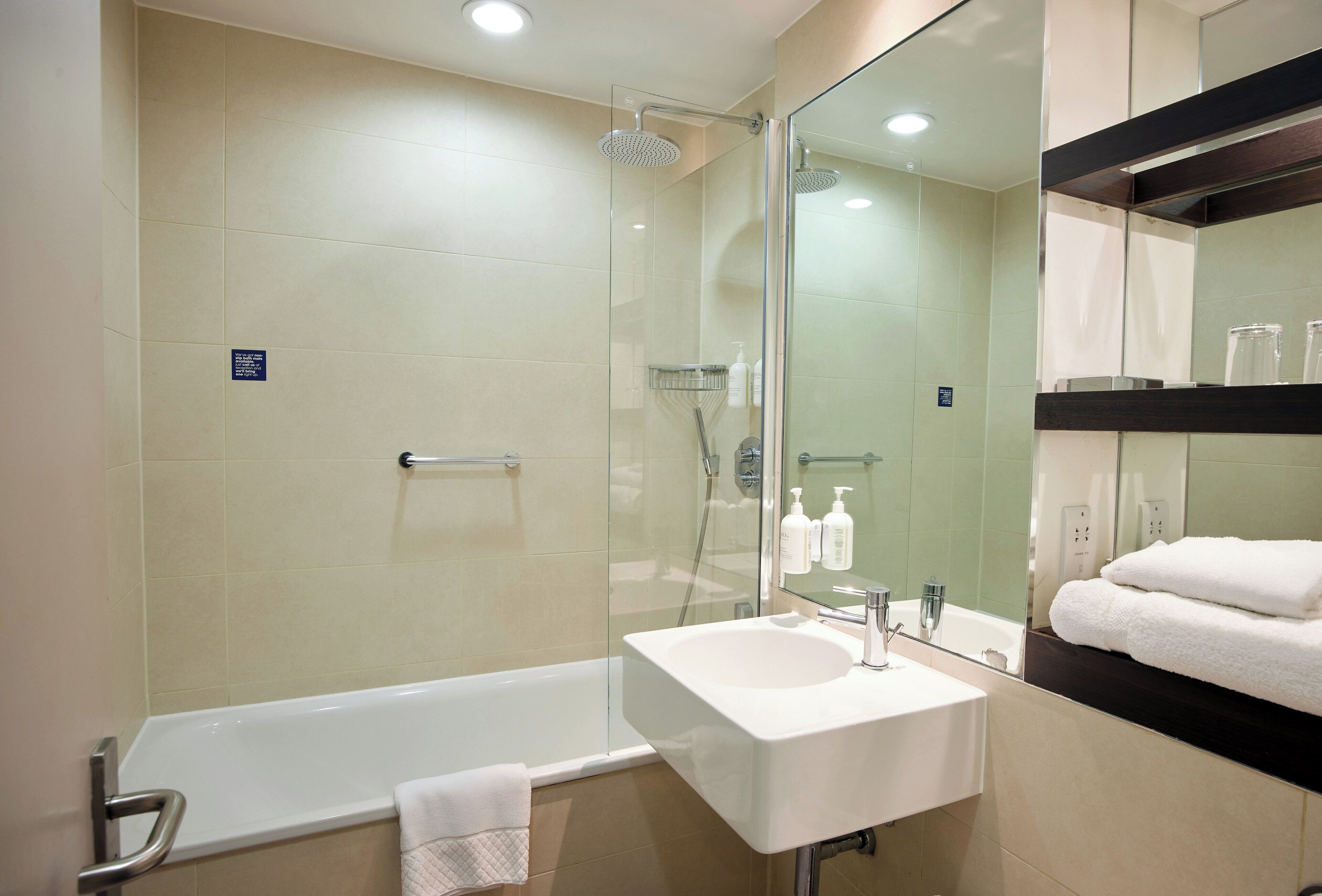 A modern bathroom with a glass-enclosed shower, a white sink, and a large mirror.